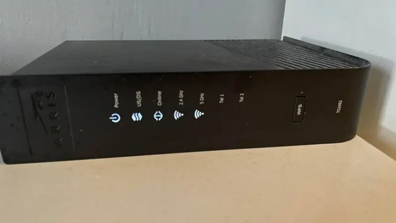 Czarny router Arris TG2492 z widocznym przyciskiem WPS i wskaźnikami stanu: Power, US/DS, Online, 2.4 GHz, 5 GHz, Tel 1, Tel 2.